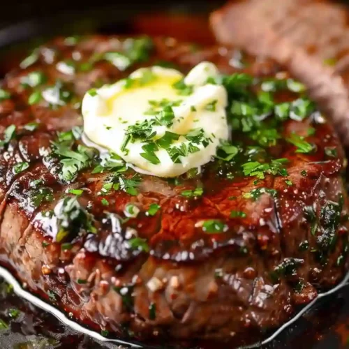 Extra close-up pan-seared filet mignon topped with melted herb butter in a dark skillet