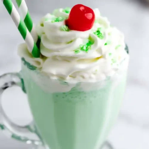 Extra close-up Shamrock Shake in a clear glass mug with whipped cream, green sprinkles, and a cherry on top