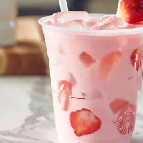 Close-up of homemade Starbucks Pink Drink in a clear plastic cup with ice and fresh strawberry slices on a marble countertop