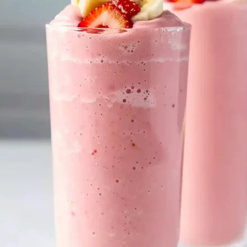 Extra close-up strawberry banana smoothie in tall glass with soft pink color on neutral background