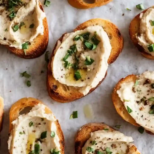 White bean crostini appetizers topped with creamy white bean spread and herbs on toasted bread slices