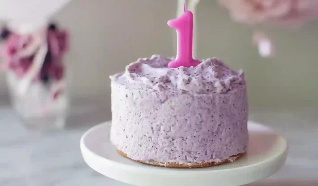 Purple frosted first birthday smash cake with pink number one candle on cake stand