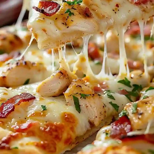 Close-up slice of chicken bacon ranch pizza with stretchy melted cheese on parchment paper
