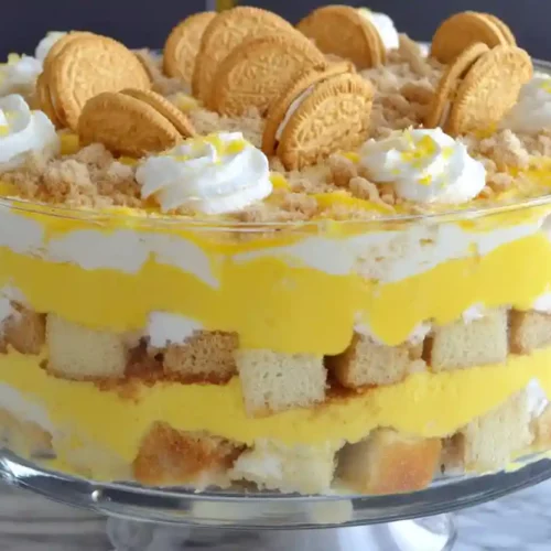 Layered lemon trifle with sponge cake, lemon custard, whipped cream, and vanilla sandwich cookies in a glass bowl