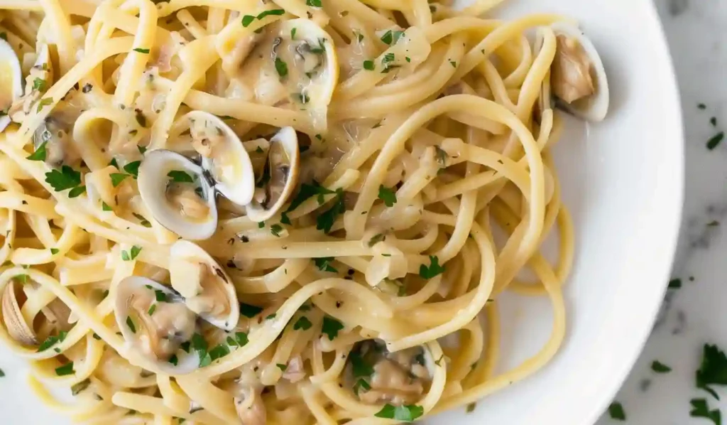 Overhead close-up of linguine with creamy white clam sauce and parsley on a white plate