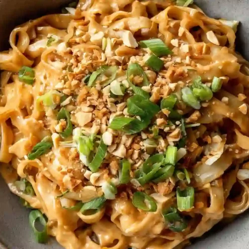 Close-up of Thai peanut noodles in a gray bowl with creamy sauce and toppings
