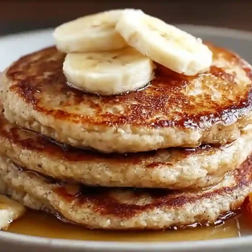 Close-up stack of banana oatmeal pancakes topped with banana slices, syrup, and strawberries