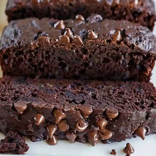 Moist chocolate zucchini bread slices on a wooden board with crumbs and chocolate chips
