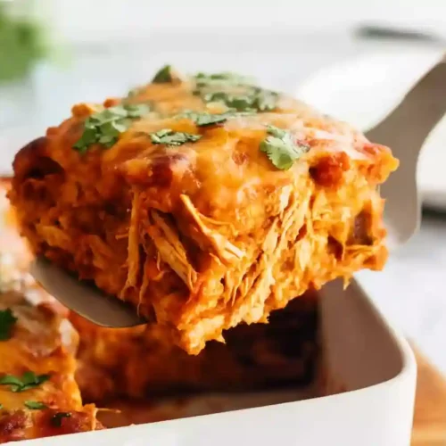 Close-up of a cheesy chicken enchilada casserole slice served on a spatula.