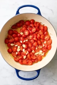 Caprese Orzo 8 Cherry tomatoes and sliced garlic cooking in olive oil in a cream Dutch oven for Caprese Orzo.