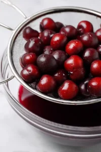Greek Yogurt with Cherry Spoon Sweets 10 Frozen dark cherries thawing in a fine-mesh strainer set over a glass bowl to collect their natural juices.